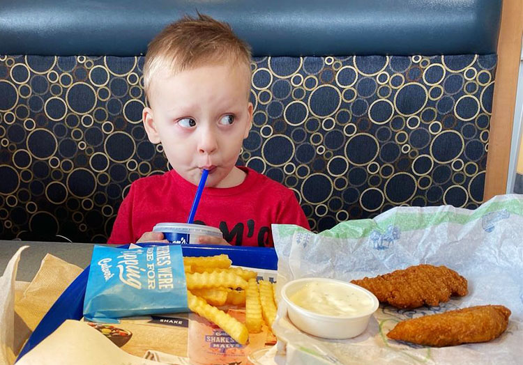 Young boy sits in a Culver’s restaurant booth with his Chicken Tender meal.